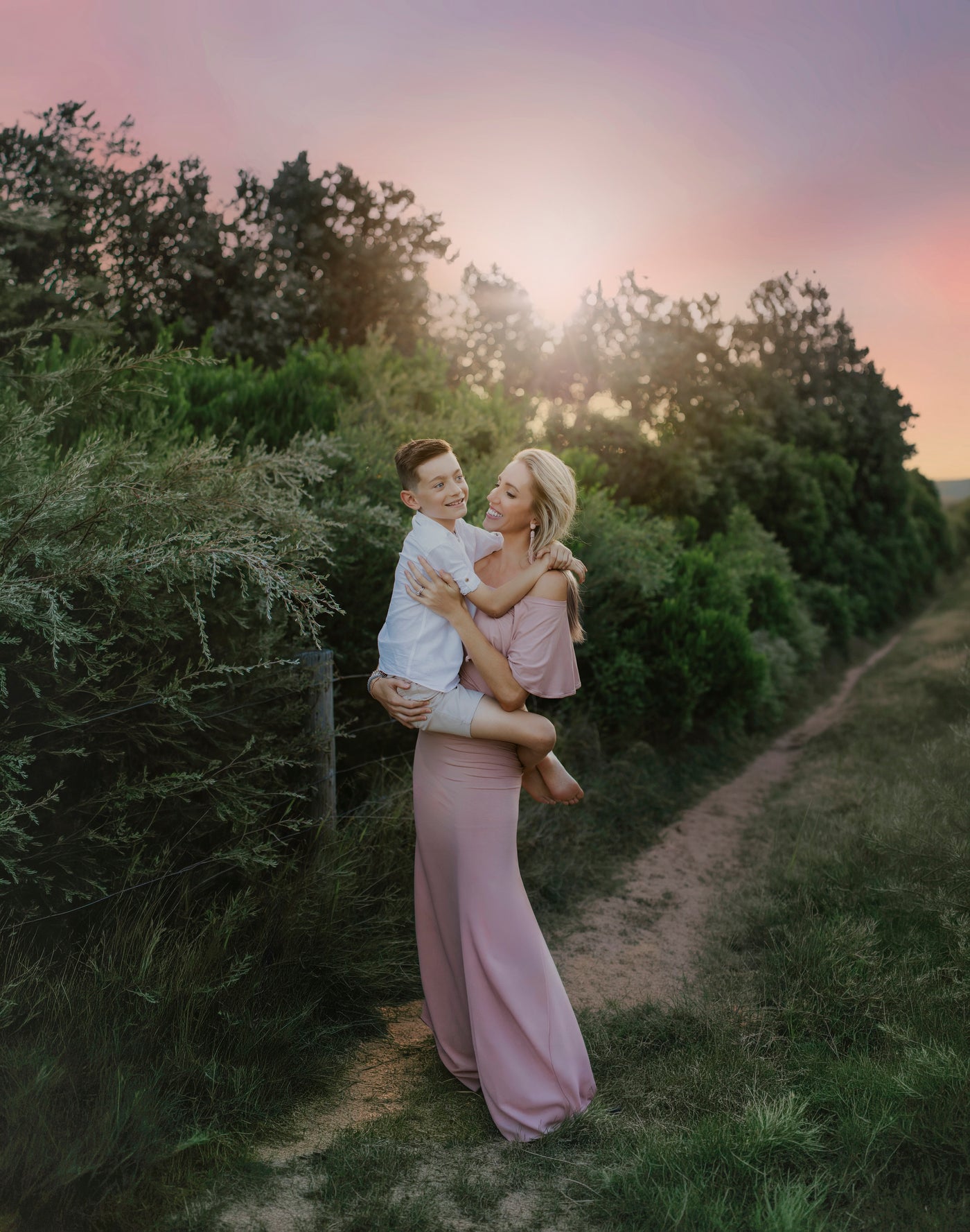 Woman in a pink dress holding a child in a field with a sunset in the background