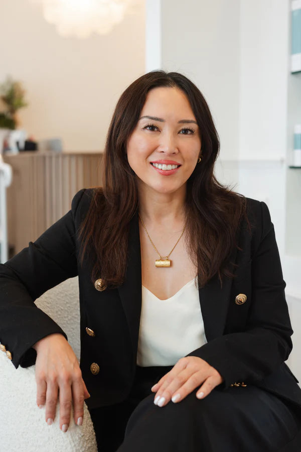 Woman in a black blazer sitting on a white couch in an indoor setting