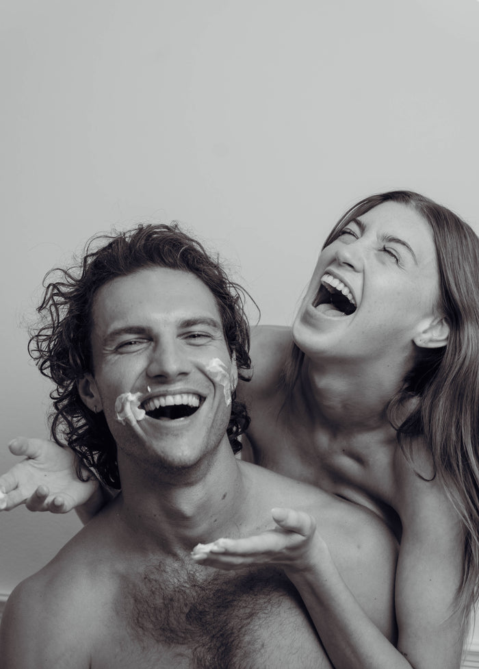 Black and white photo of a couple laughing with cream on their faces.