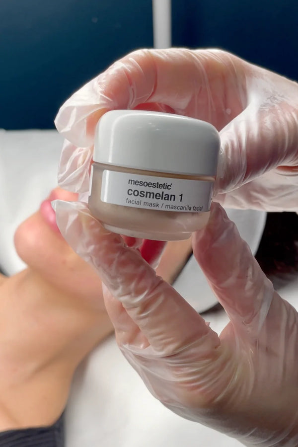 Person wearing gloves holding a small white container labeled 'cosmelan 1' against a blurred background.